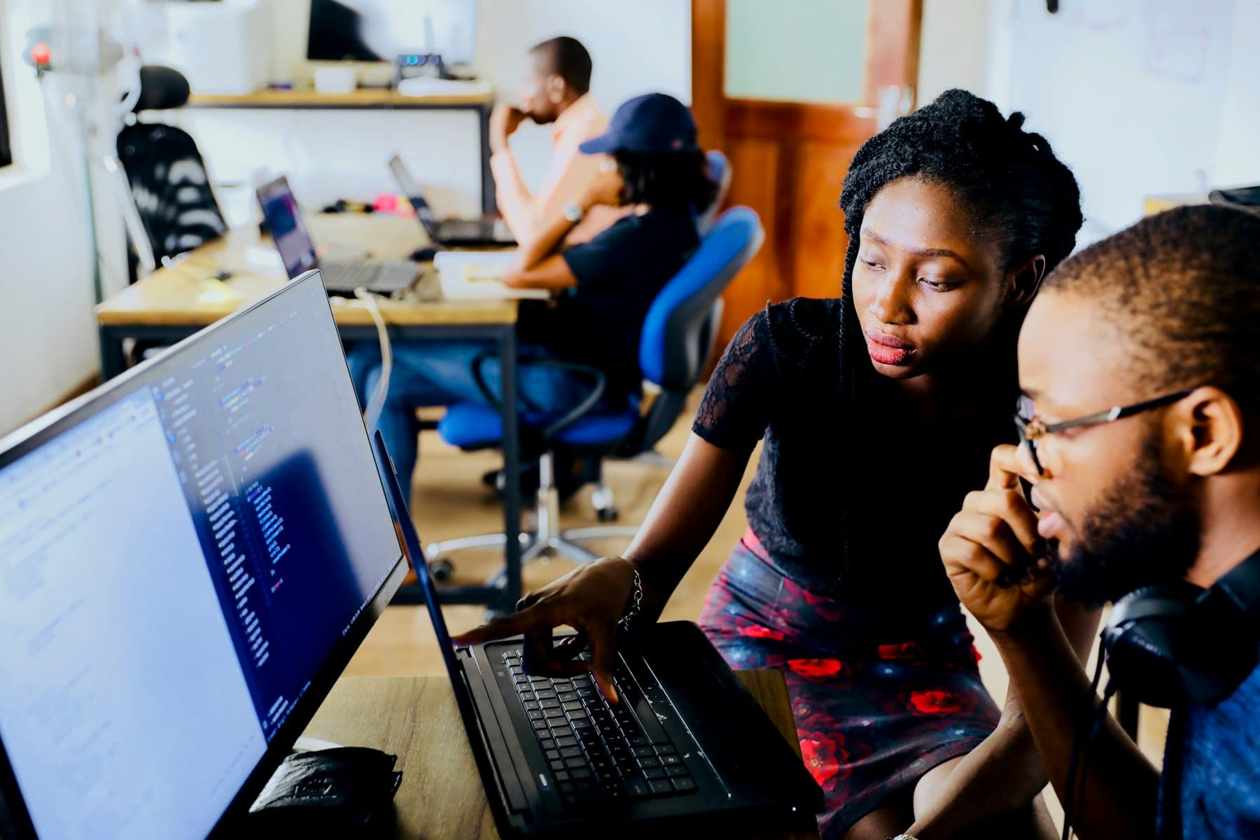 Two engineers reviewing code together on a laptop and monitor in an open office